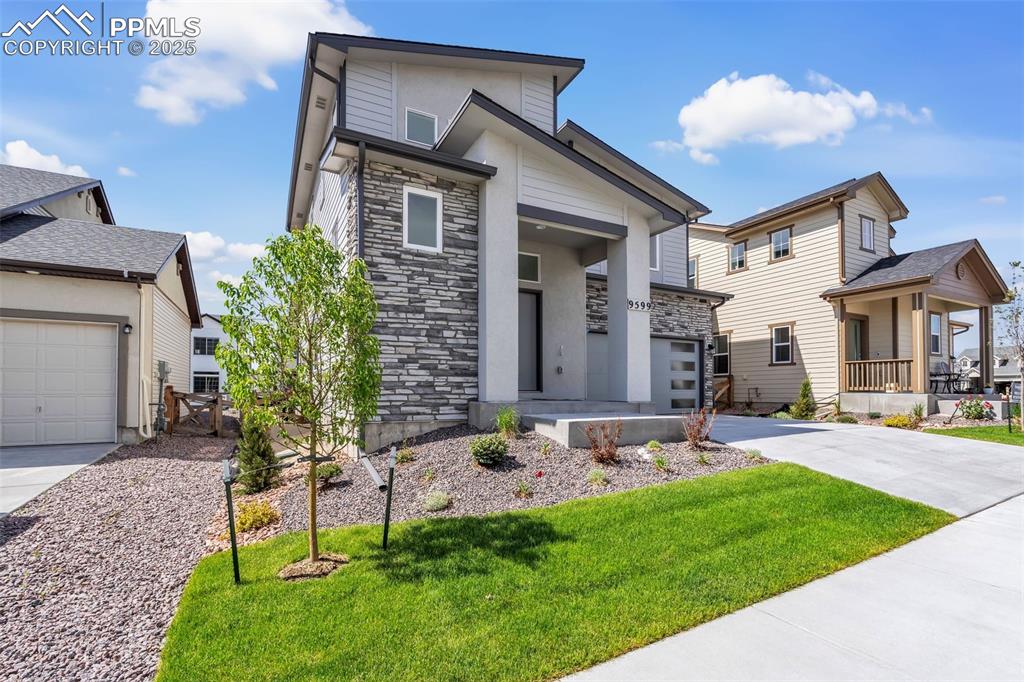 View of front facade with stone siding, a front yard, driveway, and a garage