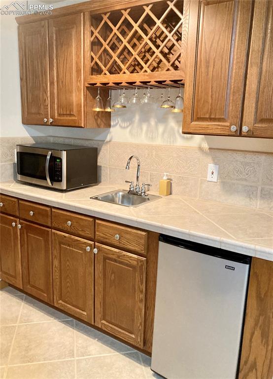 The basement wet bar boasts a tiled countertop & backsplash, wine rack and mini fridge (included).