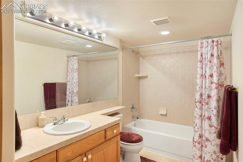 Large full bath in basement features tiled vanity countertop, tiled tub/shower surround and tile flooring.