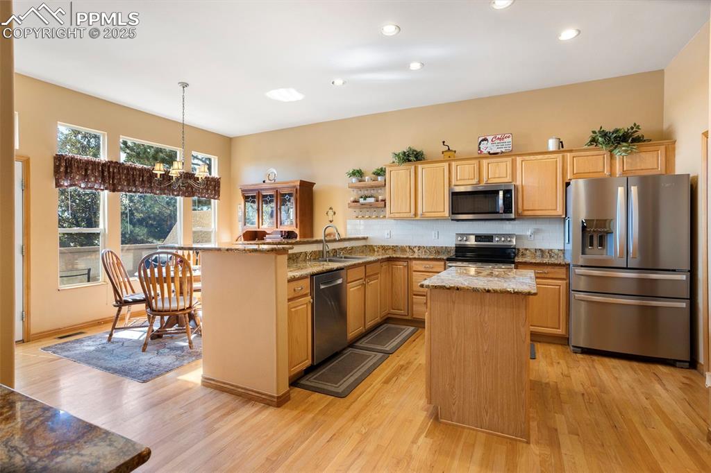 This eat-in country kitchen is a chef's dream with its center island, warm maple cabinets, slab granite counters, tiled backsplash, newer SS appliances and hardwood floors.