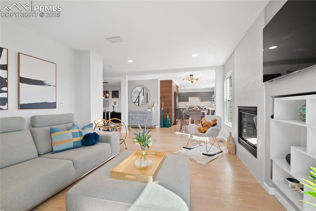 Living area featuring a glass covered fireplace, light wood-style floors, a chandelier, and recessed lighting