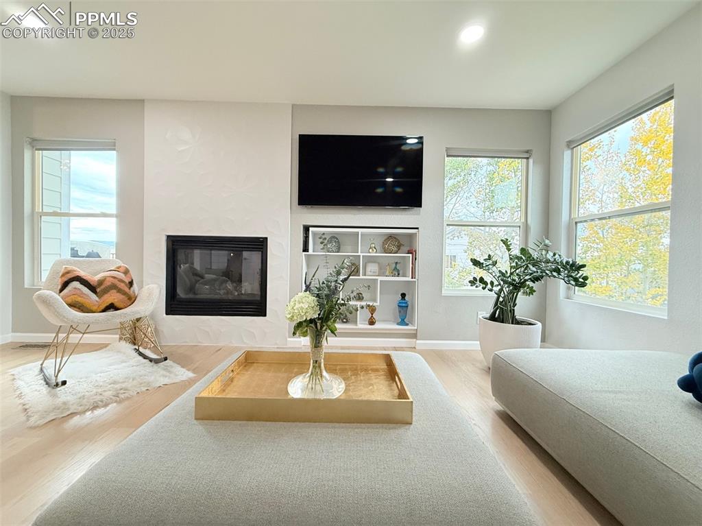Living room featuring a glass covered fireplace, plenty of natural light, light wood-type flooring, and recessed lighting