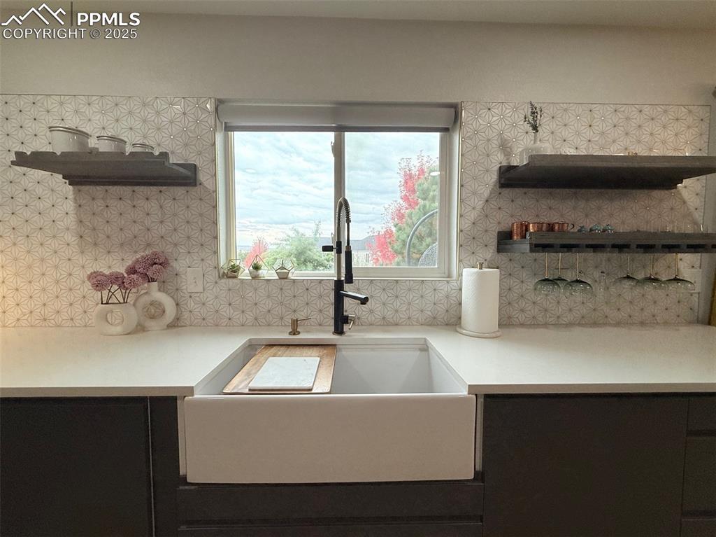 Kitchen with open shelves, tasteful backsplash, dark cabinetry, and light stone counters