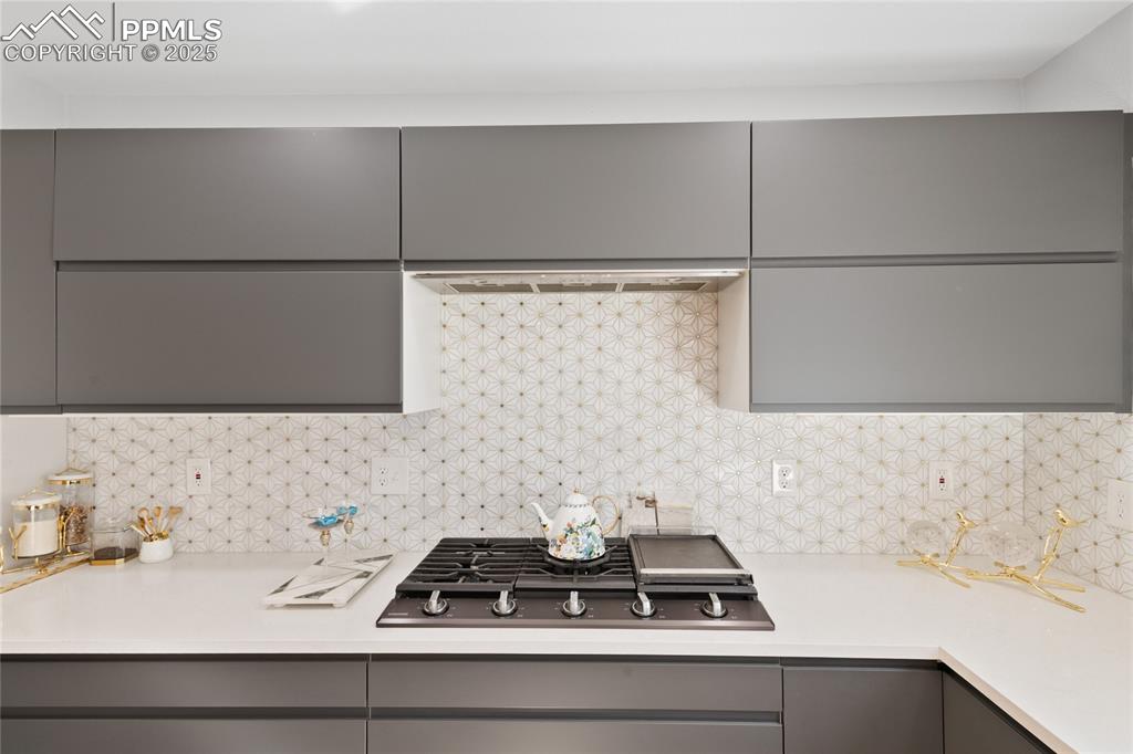 Kitchen with gray cabinetry, backsplash, black gas cooktop, modern cabinets, and extractor fan