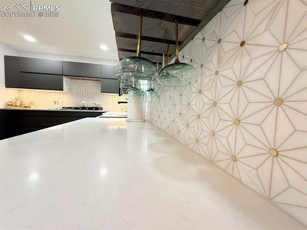 Kitchen with dark cabinets, tasteful backsplash, light stone countertops, and modern cabinets