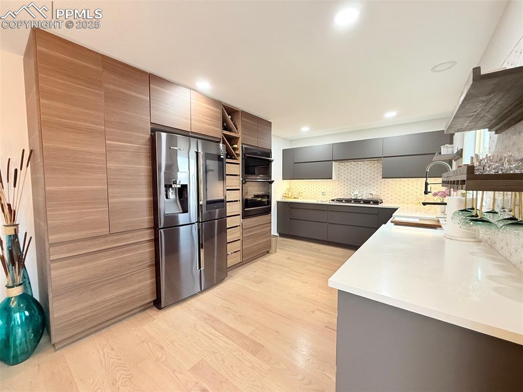 Kitchen with appliances with stainless steel finishes, light wood-type flooring, modern cabinets, open shelves, and light stone counters