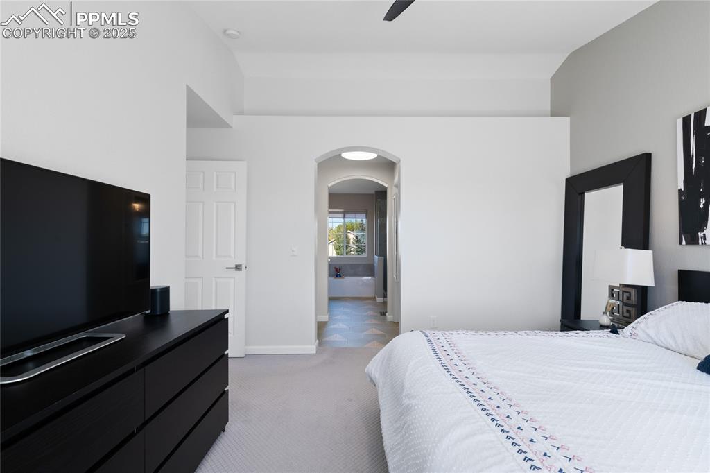 Bedroom with arched walkways, light carpet, ensuite bath, and a ceiling fan