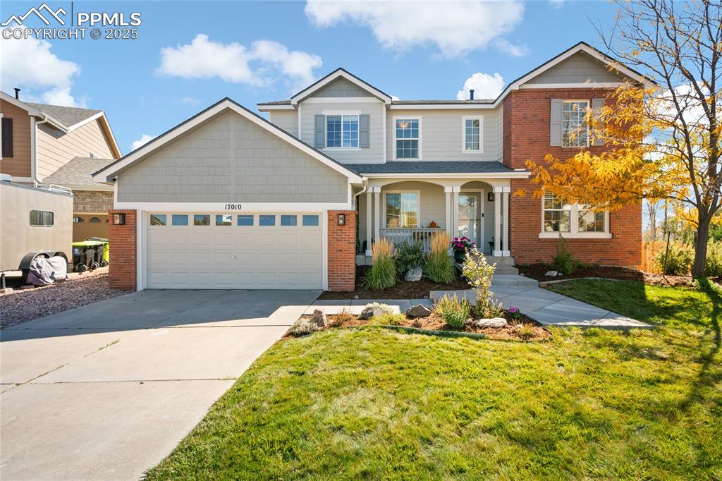 Traditional-style house featuring covered porch, concrete driveway, a front yard, brick siding, and a garage