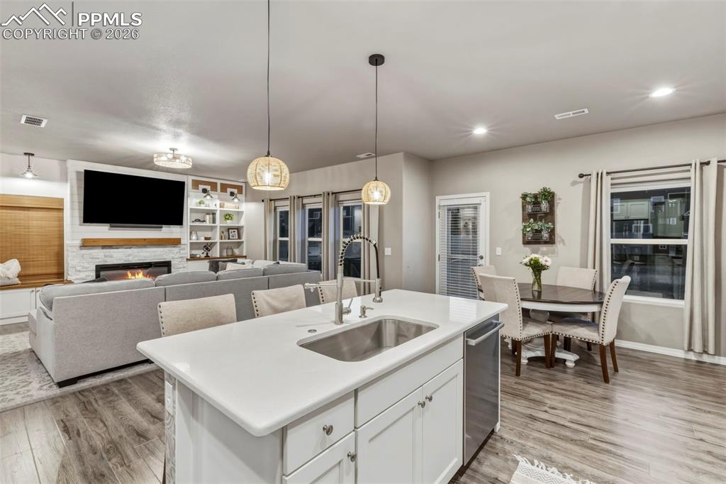 Kitchen with white cabinetry, a warm lit fireplace, a kitchen island with sink, pendant lighting, and light wood-type flooring