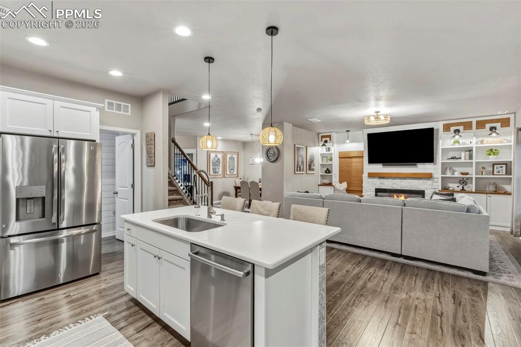 Kitchen with stainless steel appliances, white cabinetry, a warm lit fireplace, an island with sink, and open floor plan