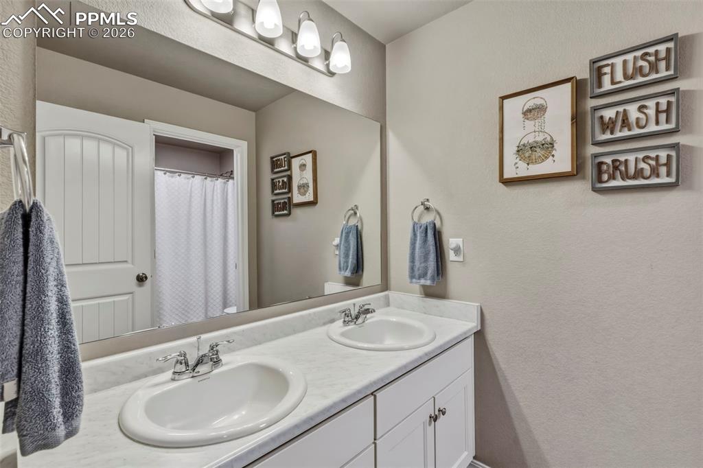 Full bath featuring a textured wall, double vanity, and a shower with shower curtain
