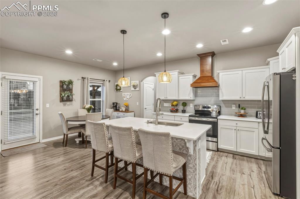 Kitchen with stainless steel appliances, white cabinets, a breakfast bar area, pendant lighting, and arched walkways