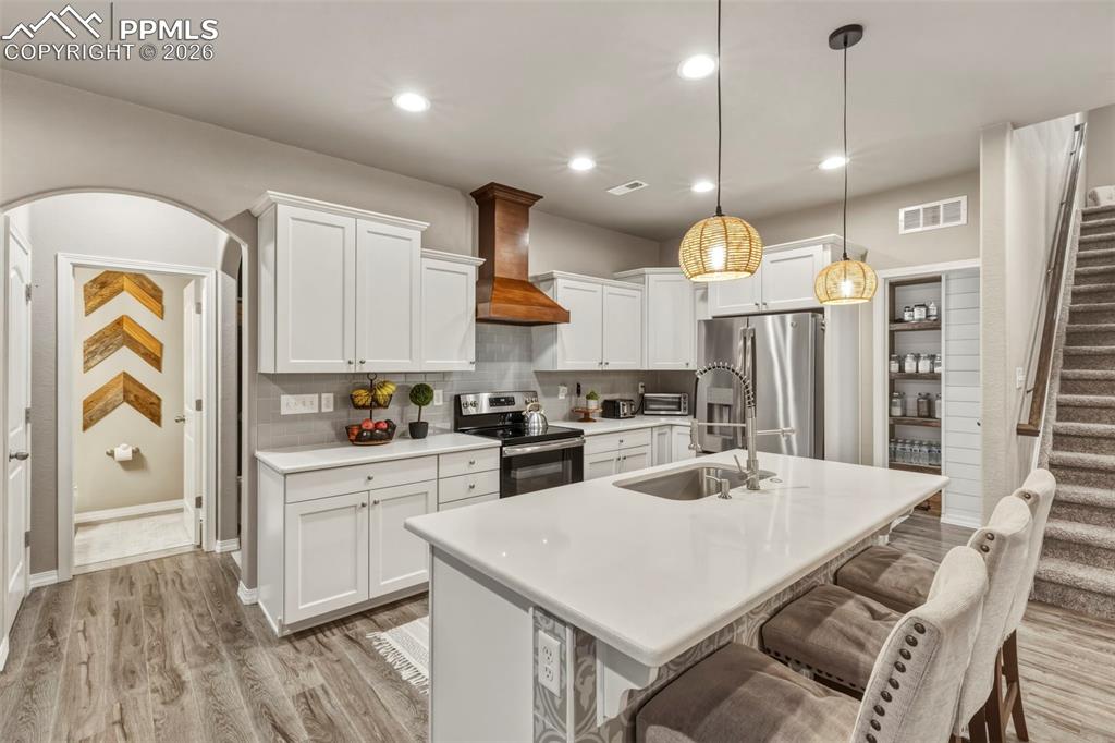 Kitchen featuring arched walkways, a breakfast bar area, white cabinets, stainless steel appliances, and a center island with sink