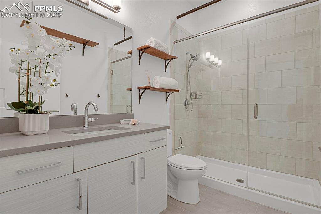 Unwind in the luxurious bathroom featuring a quartz-topped vanity, tile flooring, and 6’ full wall tiled shower with frameless glass