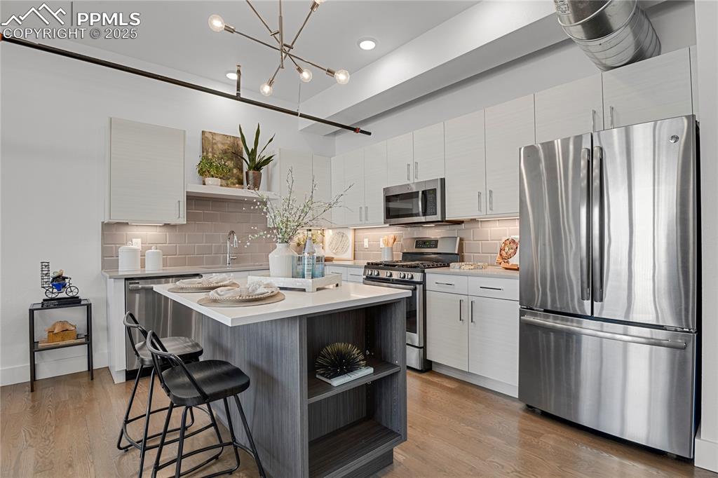 Gourmet kitchen impresses with a center island, quartz countertops, custom soft-close cabinetry, tile backsplash, and stainless steel appliances