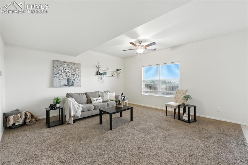 The Living Room, bathed in natural light from the large view window, features neutral carpet & a stylish lighted ceiling fan, creating an inviting space for gatherings & relaxation. 