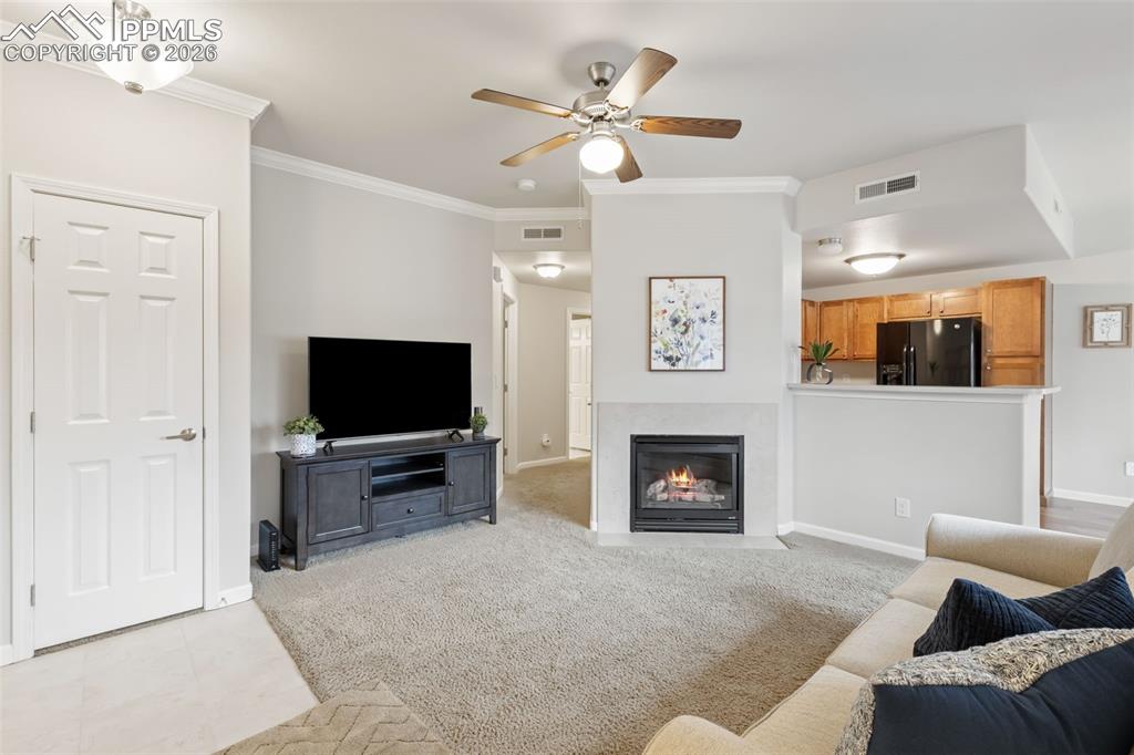 Living area with crown molding, carpet, ceiling fan, and a fireplace with flush hearth