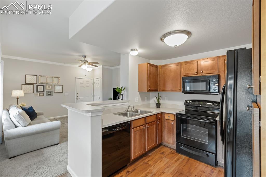 Kitchen with black appliances, wood finish cabinetry, light countertops, and crown molding