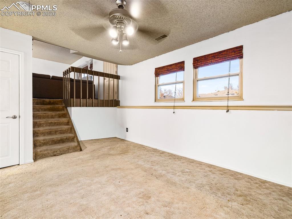 Spare room featuring ceiling fan, a textured ceiling, light carpet, a smoke detector, and stairway