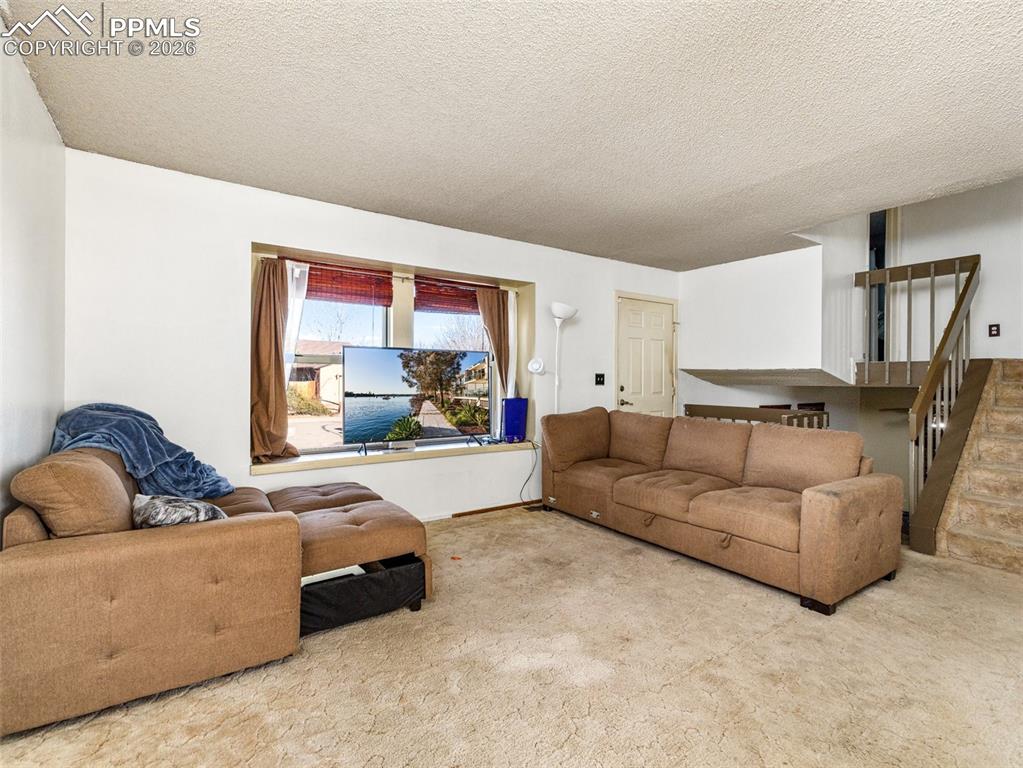 Living room featuring a textured ceiling, carpet flooring, and stairs