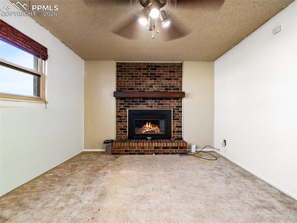 Unfurnished living room with a fireplace, a textured ceiling, carpet, and a ceiling fan