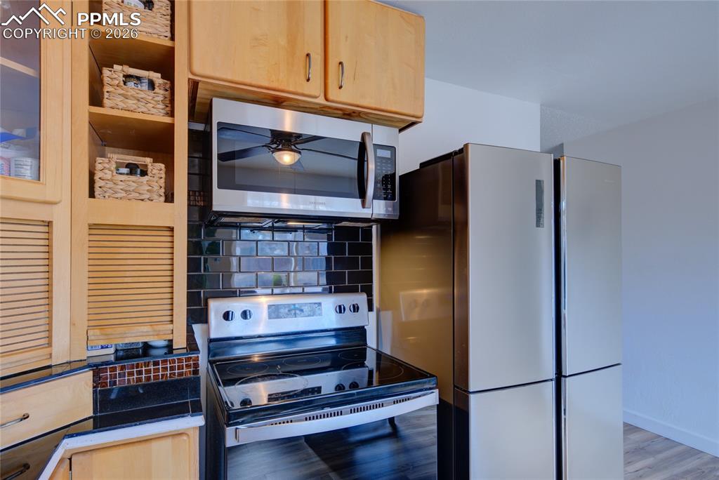 Kitchen with electric range oven, stainless steel microwave, tasteful backsplash, and light wood finish cabinetry