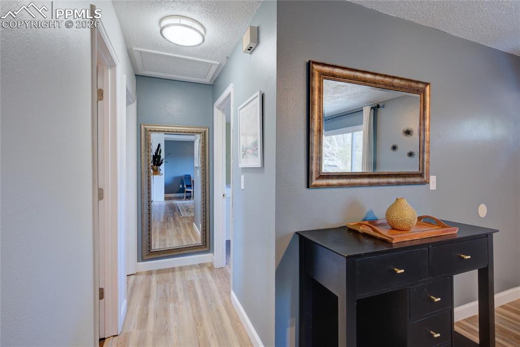 Hall with a textured ceiling, light wood-style floors, and a textured wall