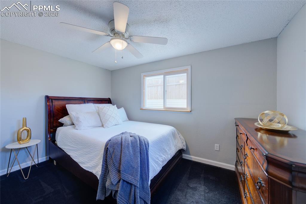 Bedroom with a textured ceiling, ceiling fan, and dark colored carpet