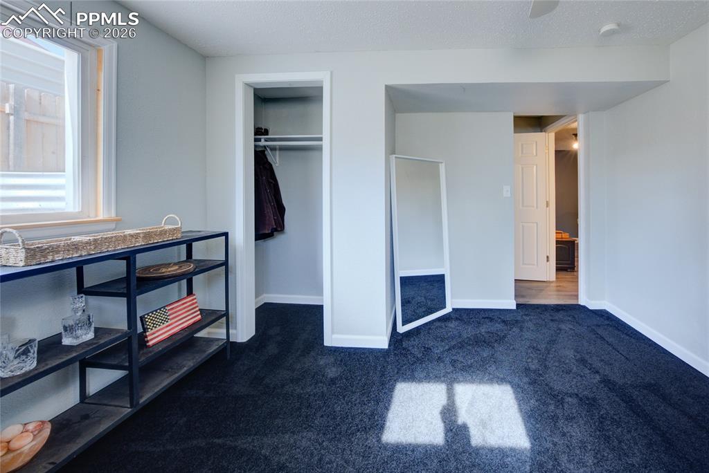 Unfurnished bedroom featuring dark colored carpet, a closet, a ceiling fan, and a textured ceiling