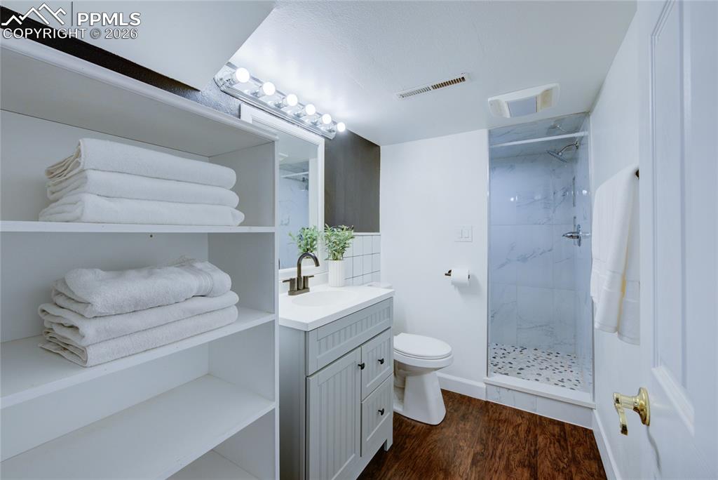 Bathroom with vanity, a marble finish shower, and dark wood-style floors