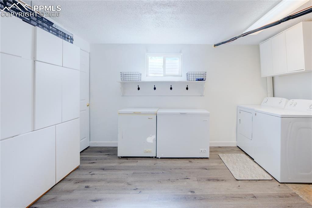 Laundry room featuring a textured ceiling, light wood-style floors, separate washer and dryer, and cabinet space