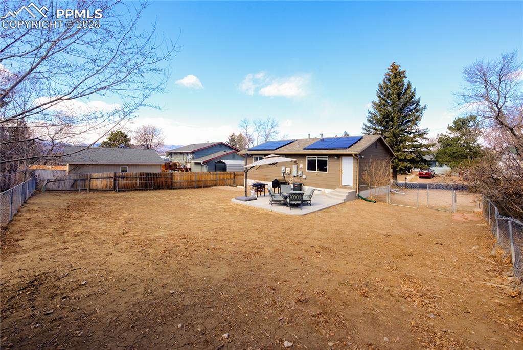 Back of house featuring a patio, solar panels, a fenced backyard, and a gate