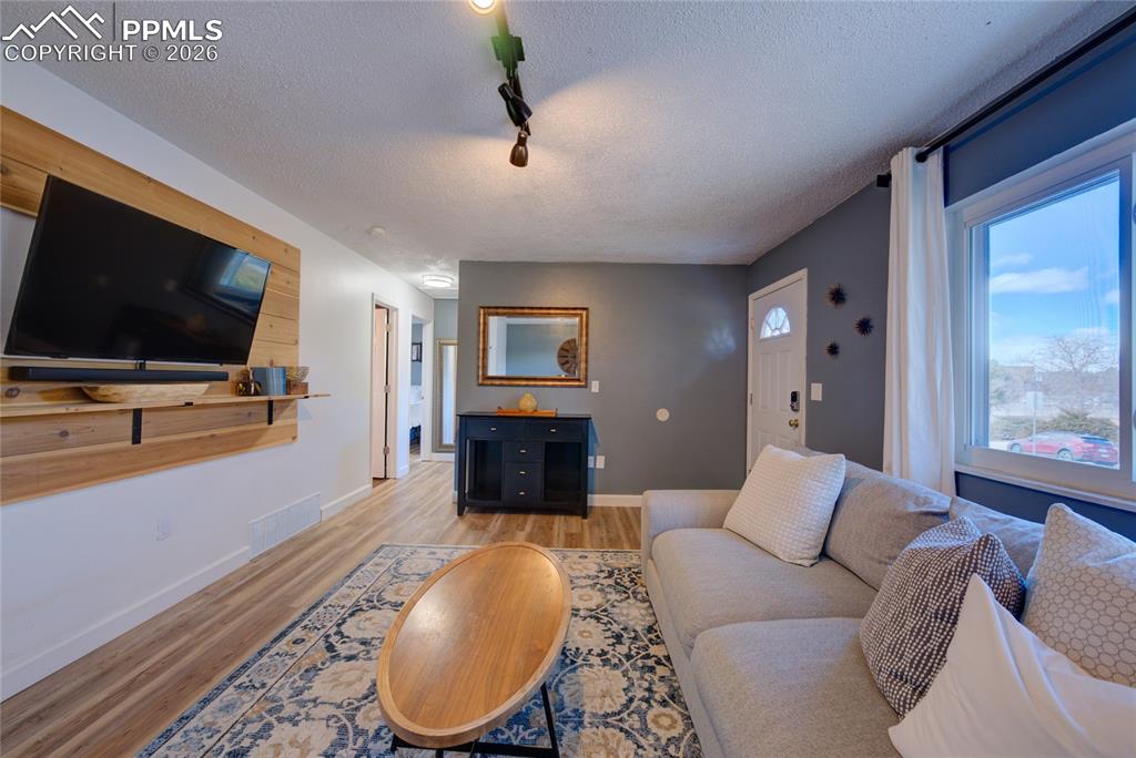 Living room with a textured ceiling, track lighting, and light wood-type flooring