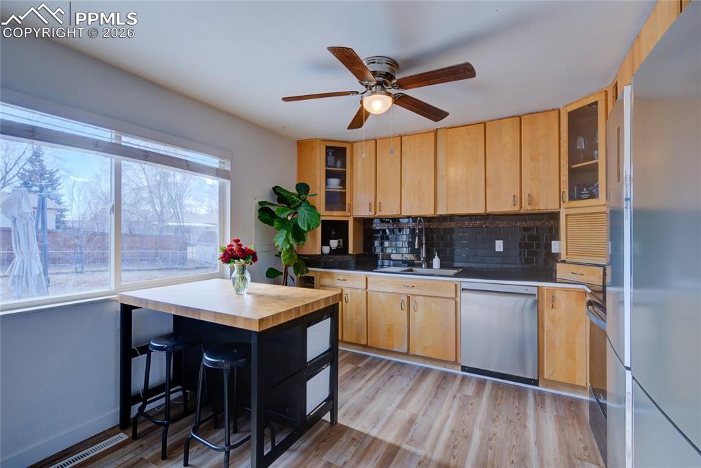 Kitchen featuring stainless steel appliances, glass fronted cabinets, light wood-style flooring, and light wood finish cabinetry