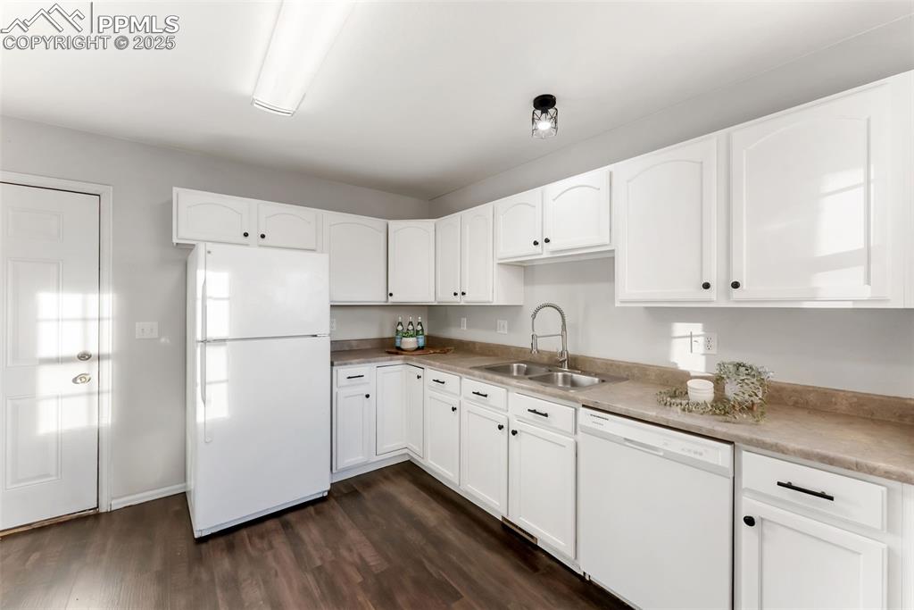 Kitchen featuring white appliances, white cabinets, dark wood-style flooring, and light countertops