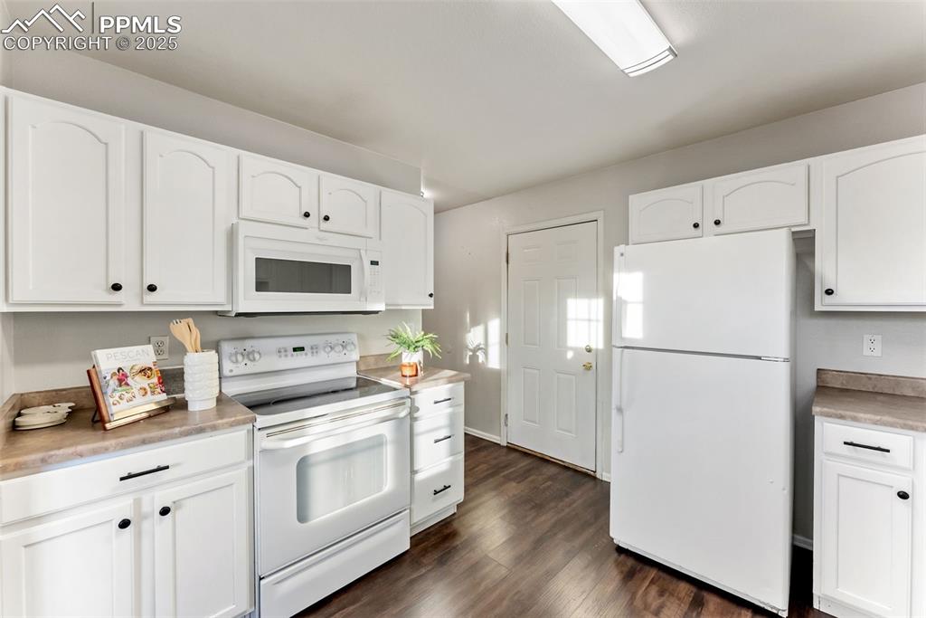 Kitchen featuring white appliances, white cabinets, dark wood-style flooring, and light countertops