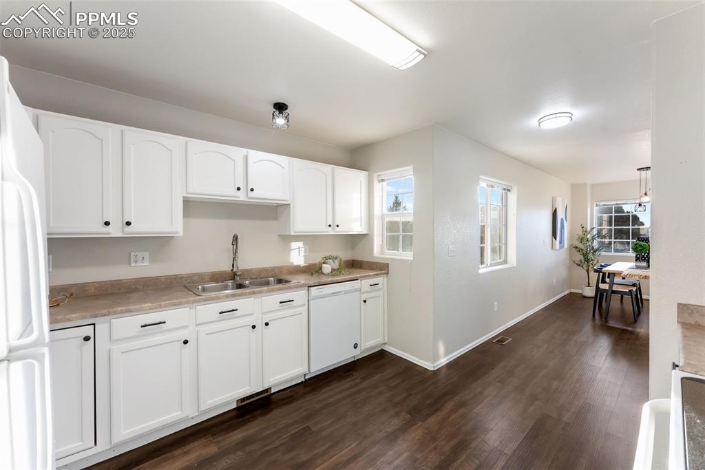 Kitchen featuring white appliances, white cabinets, dark wood finished floors, and plenty of natural light
