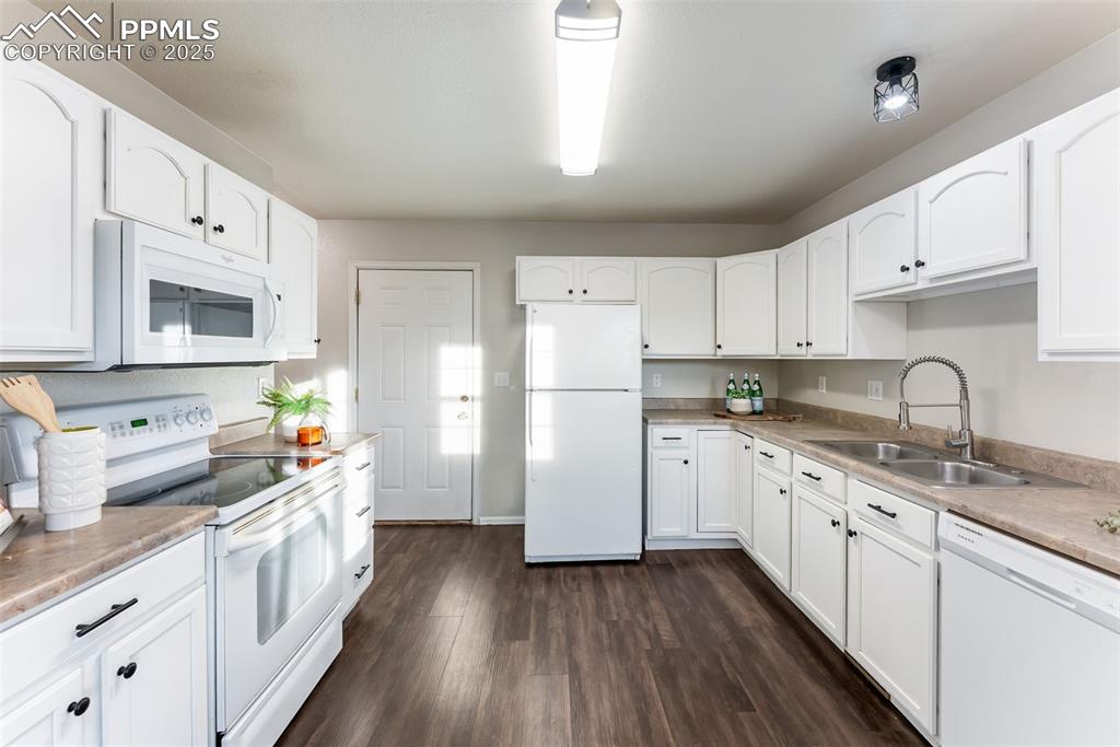 Kitchen with white appliances, white cabinets, dark wood-style floors, and light countertops