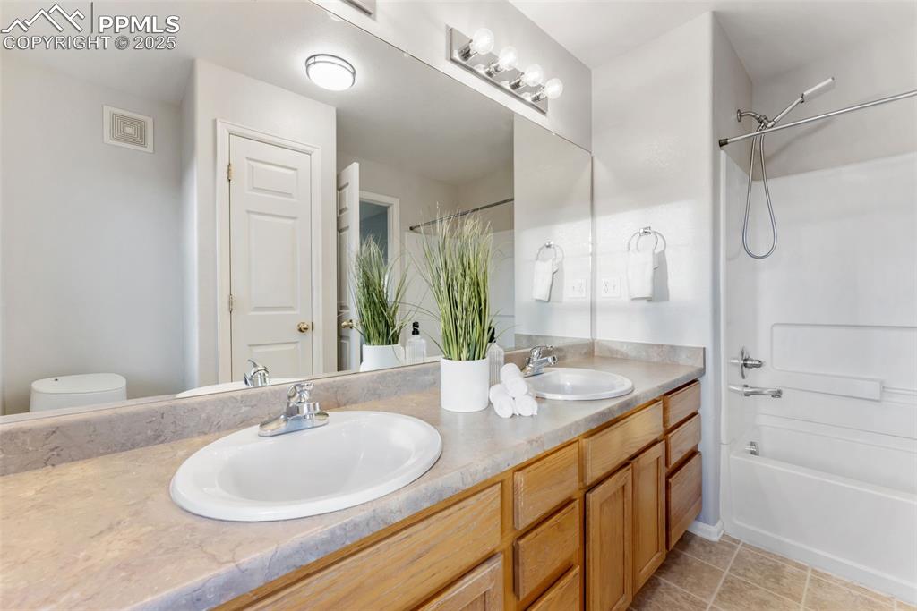 Bathroom with double vanity, shower / tub combo with curtain, and light tile patterned floors