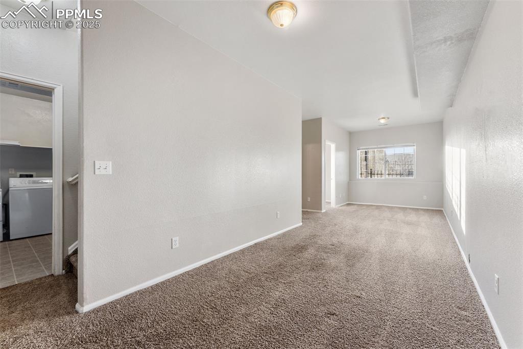 Carpeted empty room featuring washer / dryer and a textured wall