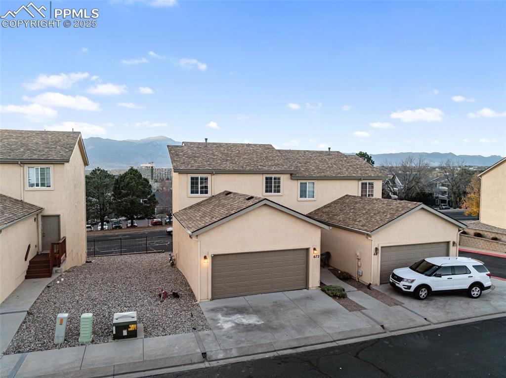 Traditional-style home with a mountain view, stucco siding, driveway, an attached garage, and a shingled roof