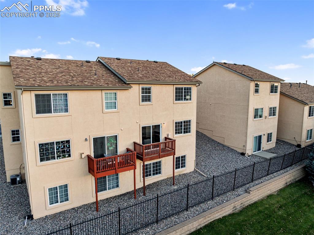 Back of house featuring a shingled roof, stucco siding, a fenced backyard, and a wooden deck