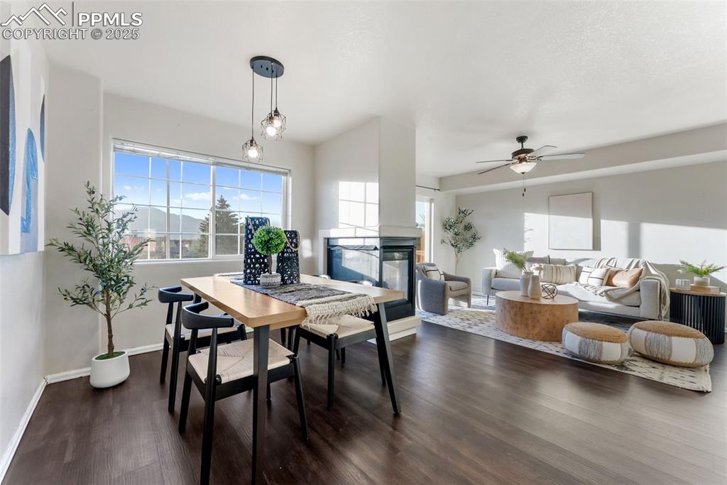 Dining area featuring a multi sided fireplace, dark wood finished floors, and a ceiling fan