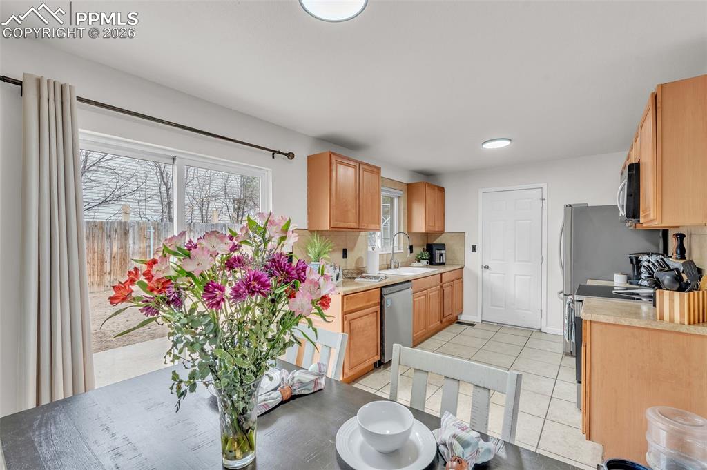 Kitchen featuring stainless steel appliances, light tile patterned floors, light wood finish cabinetry, and backsplash