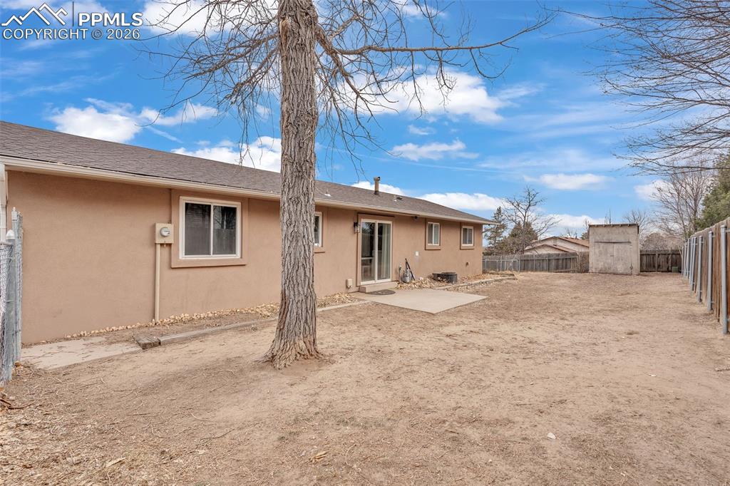 Rear view of house featuring stucco siding, a fenced backyard, a storage shed, and a patio