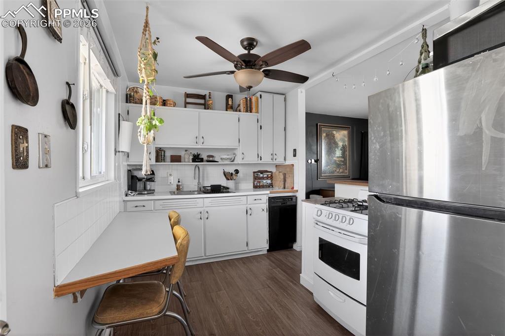 Kitchen with freestanding refrigerator, light countertops, white cabinets, white range with gas stovetop, and backsplash