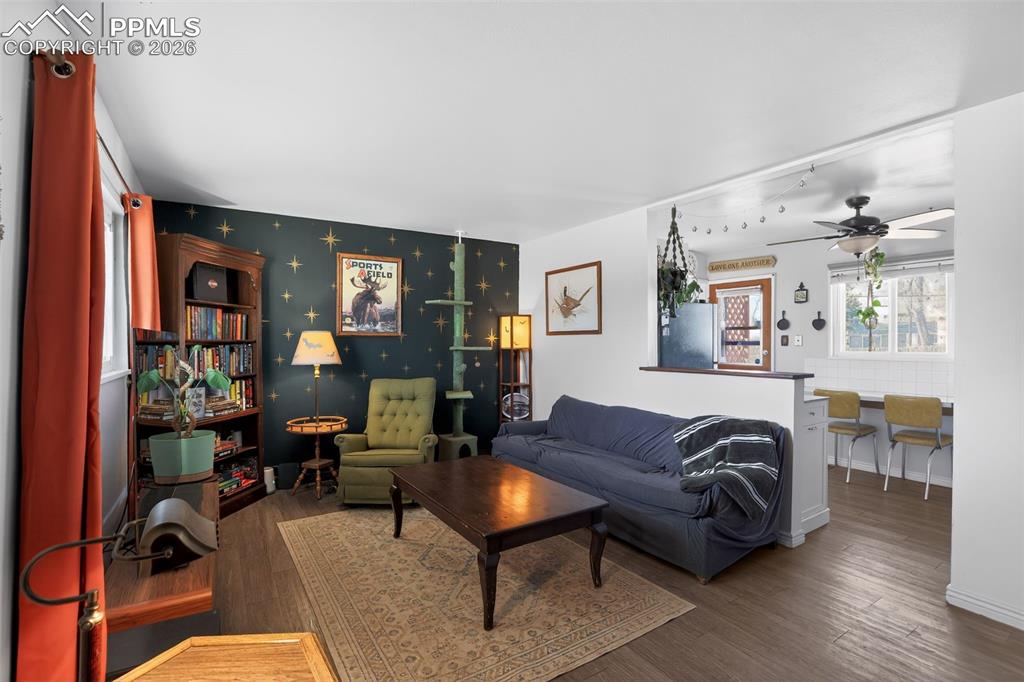 Living area featuring wallpapered walls, an accent wall, wood finished floors, and ceiling fan