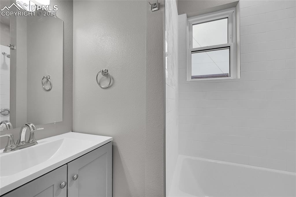 Bathroom with vanity, a textured wall, and bathtub / shower combination