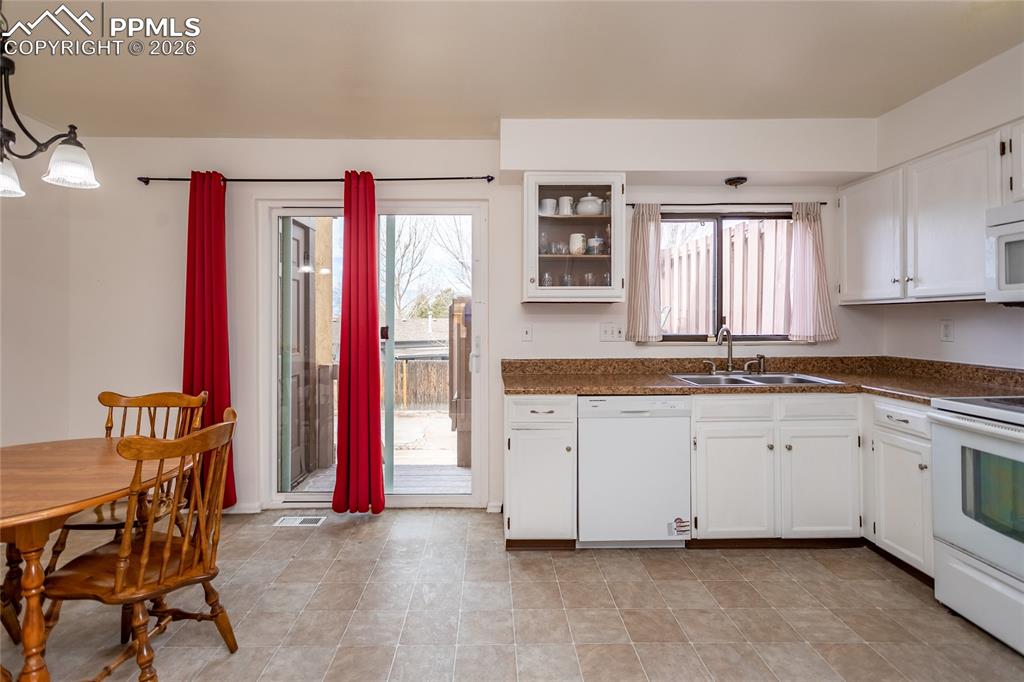 Kitchen featuring white cabinetry, white appliances, decorative light fixtures, and glass insert cabinets