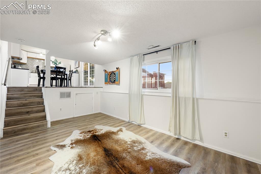 Unfurnished living room featuring a textured ceiling, light wood-type flooring, stairway, and track lighting